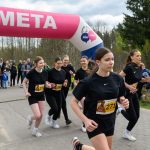 Na zdjęciu młode biegaczki biegną przez linię mety. Nad nimi różowy łuk z napisem „META”. W tle widoczni są kibice i drzewa.