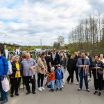 Grupa ludzi stoi na asfaltowej drodze, kilka osób trzyma medale. W tle widoczne są drzewa i pochmurne niebo. Po lewej stronie znajduje się drewniany pawilon.