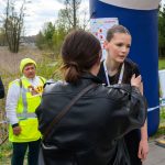 Grupa ludzi rozmawia na tle niebieskiego balonu startowego. Jedna z osób ma żółtą kamizelkę odblaskową. W tle widać zieleń i niebo.