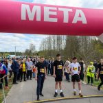 Na zdjęciu widać młodych uczestników biegu stojących pod różowo-białym łukiem z napisem META. W tle jest tłum ludzi oraz drzewa i niebo z chmurami. Po lewej znajduje się znak z informacjami o pomiarze czasu.