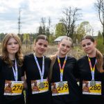 Cztery osoby w czarnych koszulkach z numerami startowymi i medalami. W tle drzewa i pochmurne niebo. Uczestnicy stoją blisko siebie.