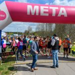 Biegacze na starcie pod różowo-niebieską bramą z napisem „META”. Słoneczny dzień, spokojne, naturalne tło z drzewami. Elektroniczny zegar wskazuje godzinę 11:28.