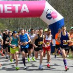 Grupa biegaczy startuje spod różowego łuku z napisem META. Ubrani w kolorowe stroje sportowe biegną po chodniku. W tle widać drzewa i widzów.