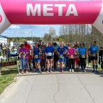 Grupa biegaczy stoi na starcie pod różowo-niebieskim łukiem mety. Na liczniku czas 00:00:43. W tle drzewa i niebo.