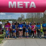 Zawodnicy stoją pod różowo-białą bramką z napisem META. Są ubrani w kolorowe stroje sportowe. W tle widać drzewa i niebo z chmurami.