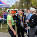 Kobieta w zielonej koszulce otrzymuje medal na zawodach. W tle namiot i drzewa. Kilka osób stojących obok z medalami.