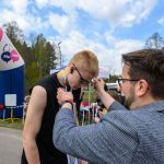 Osoba nakłada medal biegaczowi przy mecie w plenerze. W tle widoczne są drzewa i fragment różowego balonu. Na podświetlaczu widnieje czas 00:29:35.