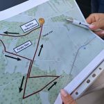 Mapa trasy pieszej z zaznaczonymi punktami Świetlica Wólka Kokojsa i Poręby Stare. Tło zielone, drogi czerwone. Ręka trzymająca długopis.