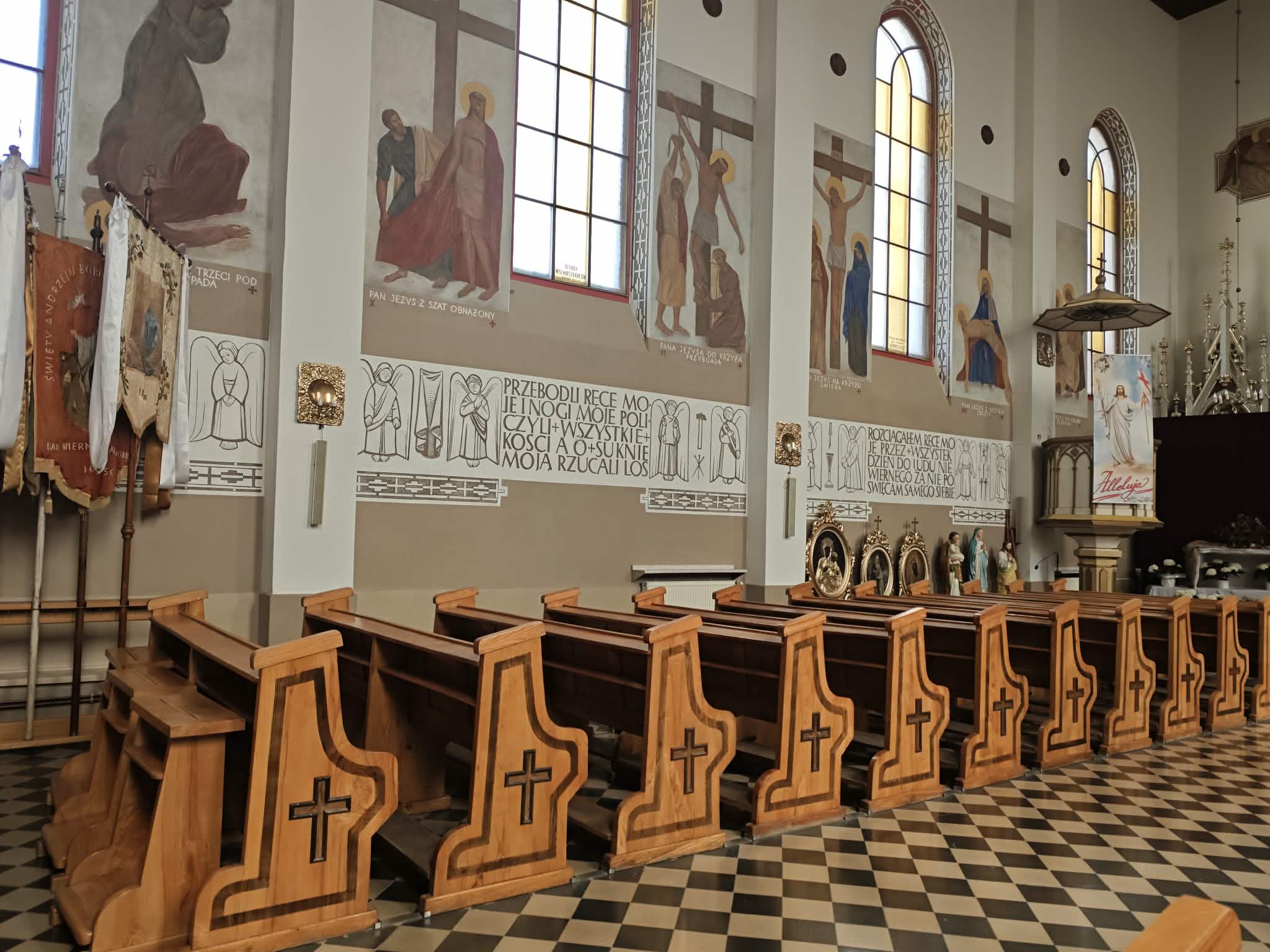 Drewniane ławki z krzyżami w kościele; na ścianach freski i witraże. Jasne wnętrze z kafelkami na podłodze.