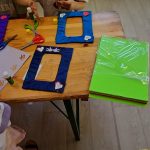 726563974_1502730784666136_6956941273025281432_n Dzieci przy stole tworzą dekoracje z papieru. Na blacie kolorowe ramki i nożyczki. Obok zielone arkusze papieru.