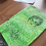 Obrazek przedstawia portret kobiety z włosami do ramion na zielonym tle. Kobieta nosi okulary i trzyma długopis. Drewniane biurko w tle.