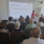 image-2227310491339619 Spotkanie w sali konferencyjnej z prezentacją Młody mimo upływu lat. Kobieta w różowej bluzce mówi do publiczności. Na ekranie widoczne logo SRCP, obok plakat z pieczywem.