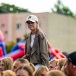 Młoda osoba w beżowej kurtce i czapce stoi w tłumie. W tle kolorowe, rozmyte budynki. Atmosfera przypomina imprezę plenerową.