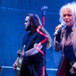 Mężczyzna gra na gitarze, kobieta śpiewa; scena oświetlona na niebiesko, tło rozmyte. Pośrodku widać czerwoną spiralę.