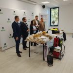 Pięć osób stoi przy stole z wyposażeniem strażackim. Tło jasne, z logotypami gminy. Obok okno, na stole ubrania i sprzęt.